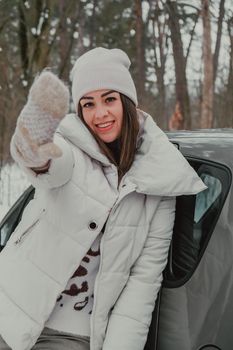 Attractive beautiful young woman in sweater staying next to the car in forest. Winter vacation. Holidays. Smilling Christmas lights.