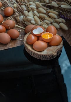 Broken chicken egg over Fresh chicken eggs (Hen eggs) placed on small timber and Dried flowers on Black table. Fresh eggs from the farmer, Natural organic healthy food concept, Copy space, Selective focus.