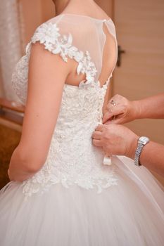 The hands of an adult woman fasten the bride's dress. Vertical photo