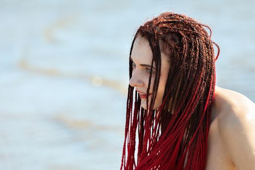 Young naked woman with scarlet dreadlocks enjoys nature by the sea