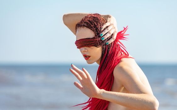 Young naked woman with scarlet dreadlocks enjoys nature by the sea