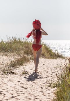 Beautiful young woman with scarlet dreadlocks and red bathing suit enjoying nature. 