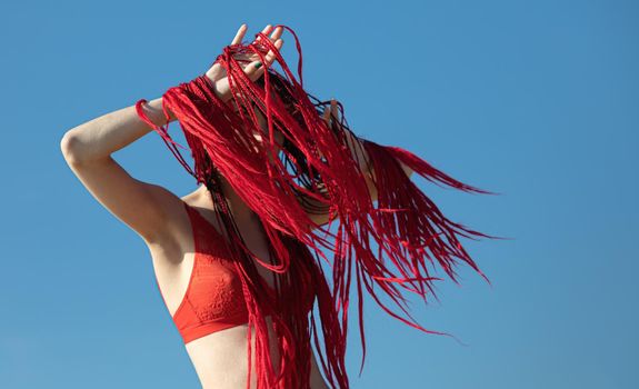 Beautiful young woman with scarlet dreadlocks and red bathing suit enjoying nature. 