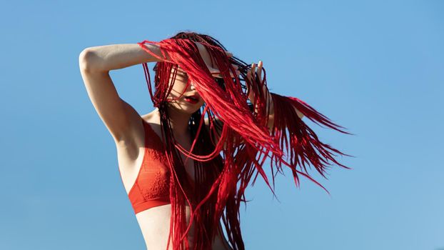 Beautiful young woman with scarlet dreadlocks and red bathing suit enjoying nature. 