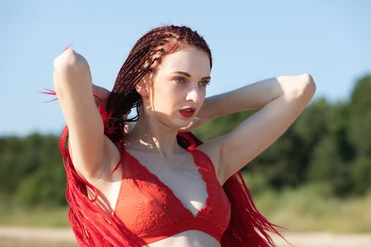Beautiful young woman with scarlet dreadlocks and red bathing suit enjoying nature. 