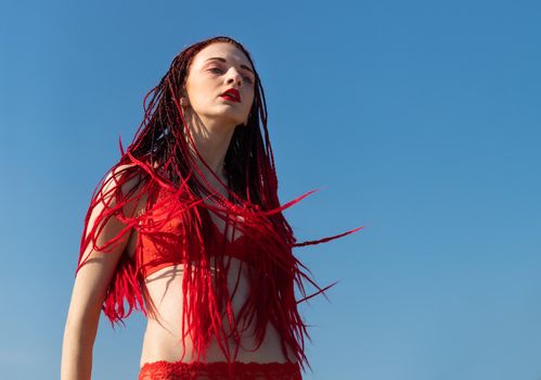 Beautiful young woman with scarlet dreadlocks and red bathing suit enjoying nature. 