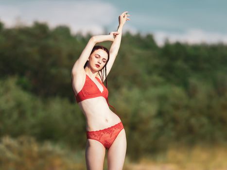 Beautiful young woman with scarlet dreadlocks and red bathing suit enjoying nature. 