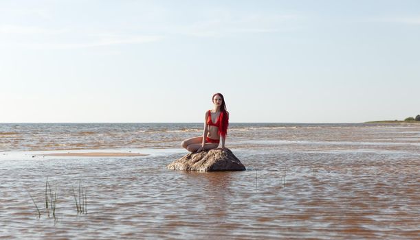 Beautiful young woman with scarlet dreadlocks and red bathing suit enjoying nature.