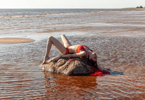 Beautiful girl outdoors enjoying nature. Seminude girl with scarlet dreadlocks in a red bathing suit sunbathes on the beach