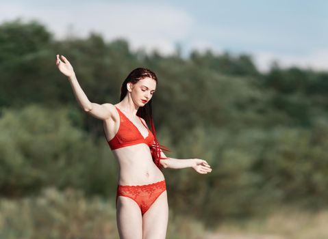 Beautiful young woman with scarlet dreadlocks and red bathing suit enjoying nature. 