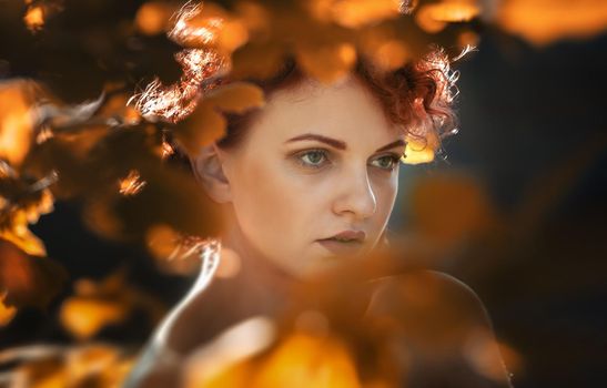 Portrait of a young red-haired young woman among the autumn foliage of trees illuminated by the suns rays
