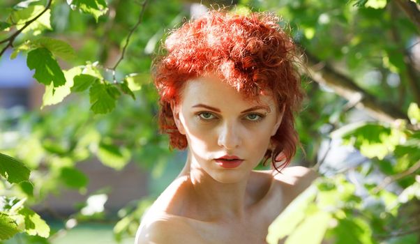 Portrait of a young red-haired woman among the foliage of trees illuminated by the suns rays