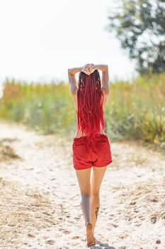 Beautiful girl outdoors enjoying nature. Seminude girl with scarlet dreadlocks in a red bathing suit sunbathes on the beach