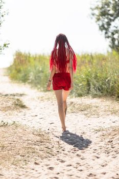 Beautiful girl outdoors enjoying nature. Seminude girl with scarlet dreadlocks in a red bathing suit sunbathes on the beach