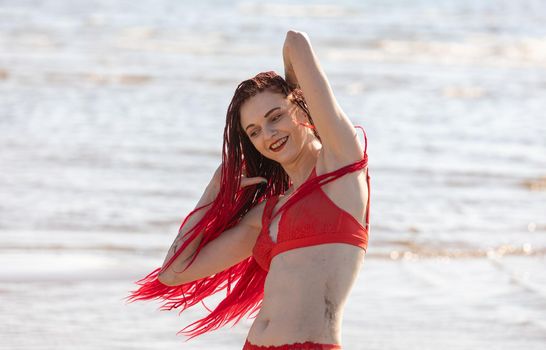 Beautiful girl outdoors enjoying nature. Seminude girl with scarlet dreadlocks in a red bathing suit sunbathes on the beach