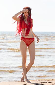 Beautiful girl outdoors enjoying nature. Seminude girl with scarlet dreadlocks in a red bathing suit sunbathes on the beach