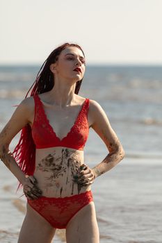 Beautiful girl outdoors enjoying nature. Seminude girl with scarlet dreadlocks in a red bathing suit sunbathes on the beach