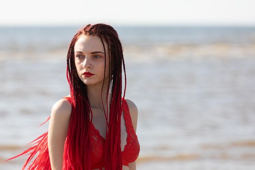 Beautiful girl outdoors enjoying nature. Seminude girl with scarlet dreadlocks in a red bathing suit sunbathes on the beach