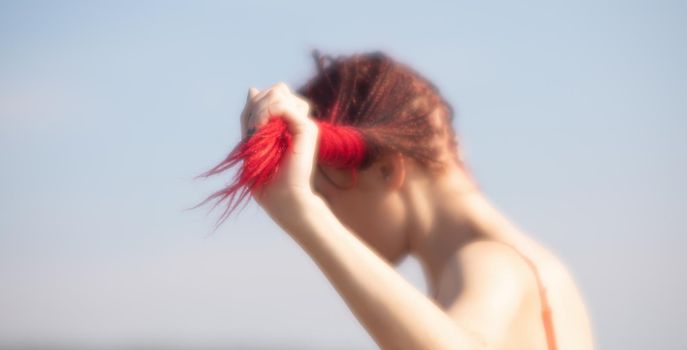 Soft focus blurred image of a beautiful young woman with scarlet dreadlocks and red bathing suit enjoying nature on the beach