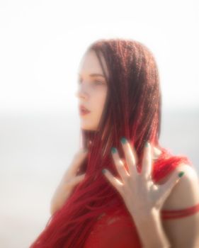 Soft focus blurred image of a beautiful young woman with scarlet dreadlocks and red bathing suit enjoying nature on the beach