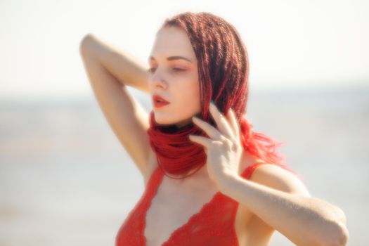 Soft focus blurred image of a beautiful young woman with scarlet dreadlocks and red bathing suit enjoying nature on the beach