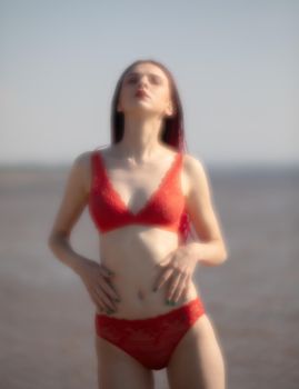 Soft focus blurred image of a beautiful young woman with scarlet dreadlocks and red bathing suit enjoying nature on the beach