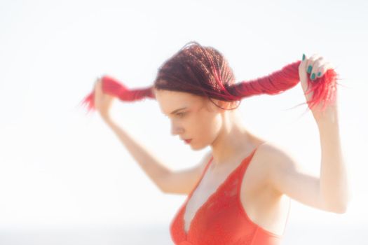 Soft focus blurred image of a beautiful young woman with scarlet dreadlocks and red bathing suit enjoying nature on the beach