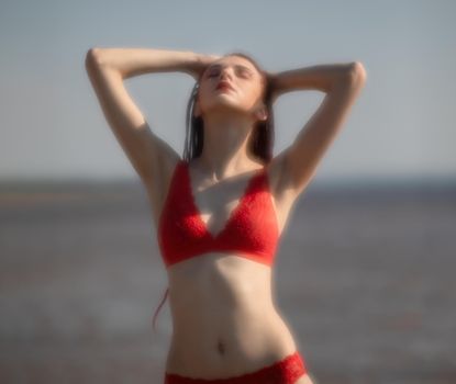 Soft focus blurred image of a beautiful young woman with scarlet dreadlocks and red bathing suit enjoying nature on the beach