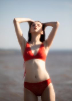 Soft focus blurred image of a beautiful young woman with scarlet dreadlocks and red bathing suit enjoying nature on the beach