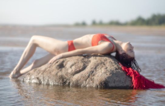 Soft focus blurred image of a beautiful young woman with scarlet dreadlocks and red bathing suit enjoying nature on the beach