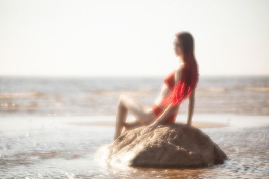 Soft focus blurred image of a beautiful young woman with scarlet dreadlocks and red bathing suit enjoying nature on the beach