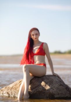 Soft focus blurred image of a beautiful young woman with scarlet dreadlocks and red bathing suit enjoying nature on the beach