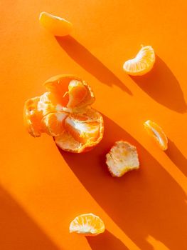 Top view of a peeled tangerine. Peel and pieces of citrus on bright orange background. Ripe fruit on sunlight.