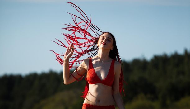 Beautiful girl outdoors enjoying nature. Seminude girl with scarlet dreadlocks in a red bathing suit sunbathes on the beach