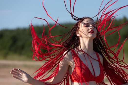 Beautiful girl outdoors enjoying nature. Seminude girl with scarlet dreadlocks in a red bathing suit sunbathes on the beach