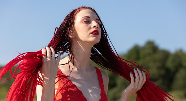 Beautiful girl outdoors enjoying nature. Seminude girl with scarlet dreadlocks in a red bathing suit sunbathes on the beach