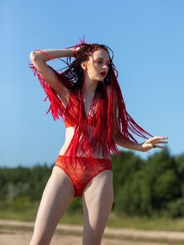 Beautiful girl outdoors enjoying nature. Seminude girl with scarlet dreadlocks in a red bathing suit sunbathes on the beach
