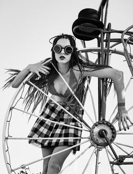 Glamorous girl with scarlet dreadlocks, a red swimsuit, black hat and welding glasses poses on the blue sky background. Free space for your text