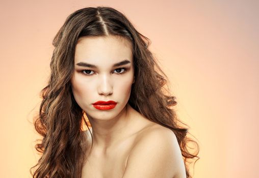 Attractive woman model on a pink background hugs herself with her hands and bright makeup brunette curls. High quality photo