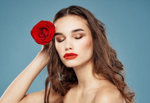 Brunette with red flower near face on blue background cropped view. High quality photo