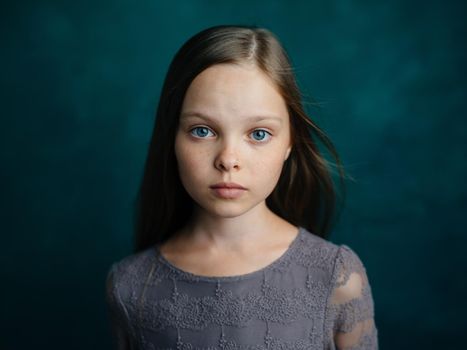 Cute blue-eyed girl in a gray dress on a green background cropped view. High quality photo