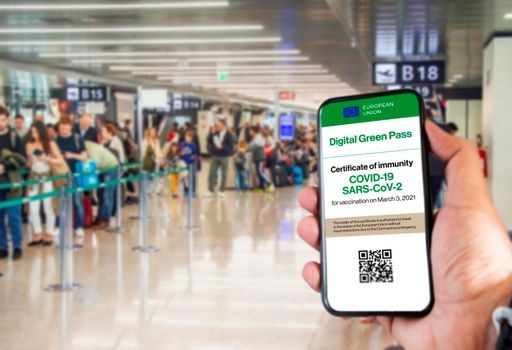 The digital green pass of the european union with the QR code on the screen of a mobile held by a hand with blurred airport in the background. Immunity from Covid-19. Travel without restrictions.