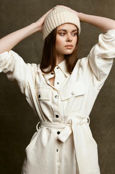 fashionable brunette in a hat and jumpsuit hold her hands behind her head on a brown background. High quality photo
