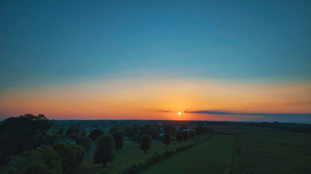 An Aerial View of a Sunset over Green Farm Lands with a Reddish Sky