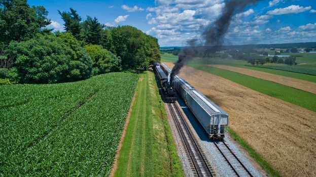 Aerial View of An Antique Restored Steam Locomotive Blowing Smoke and Steam Traveling Thru Farmlands and Countryside on a Sunny Summer Day