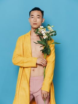 sexy man with a naked torso and in a yellow coat holding a bouquet of flowers in his hand. High quality photo