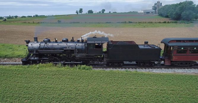 Aerial View of An Antique Restored Steam Locomotive Blowing Smoke and Steam Traveling Thru Farmlands and Countryside on a Sunny Summer Day