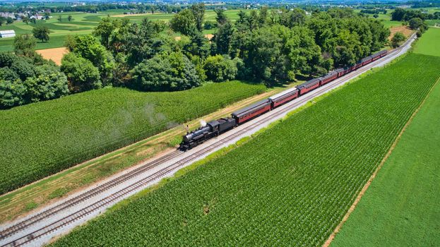 Aerial View of An Antique Restored Steam Locomotive Blowing Smoke and Steam Traveling Thru Farmlands and Countryside on a Sunny Summer Day
