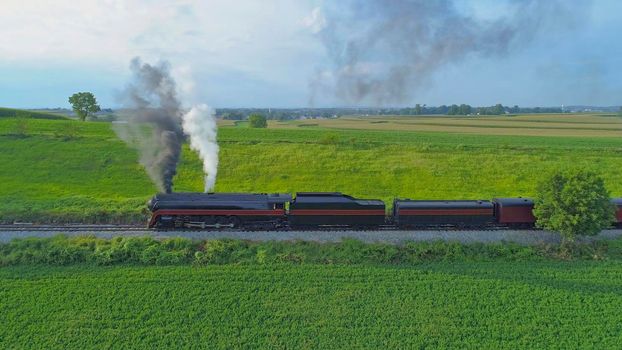 Aerial View of An Antique Restored Steam Locomotive Blowing Smoke and Steam Traveling Thru Farmlands and Countryside on a Sunny Summer Day