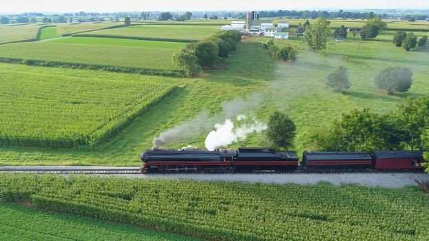 Aerial View of An Antique Restored Steam Locomotive Blowing Smoke and Steam Traveling Thru Farmlands and Countryside on a Sunny Summer Day